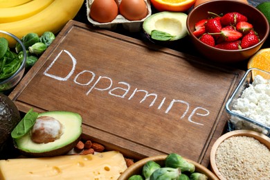 Photo of Wooden board with word Dopamine and different products as background, closeup