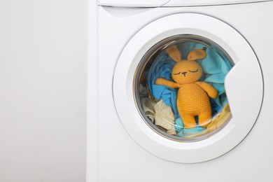 Photo of Washing machine with clothes and toy bunny near light wall, closeup