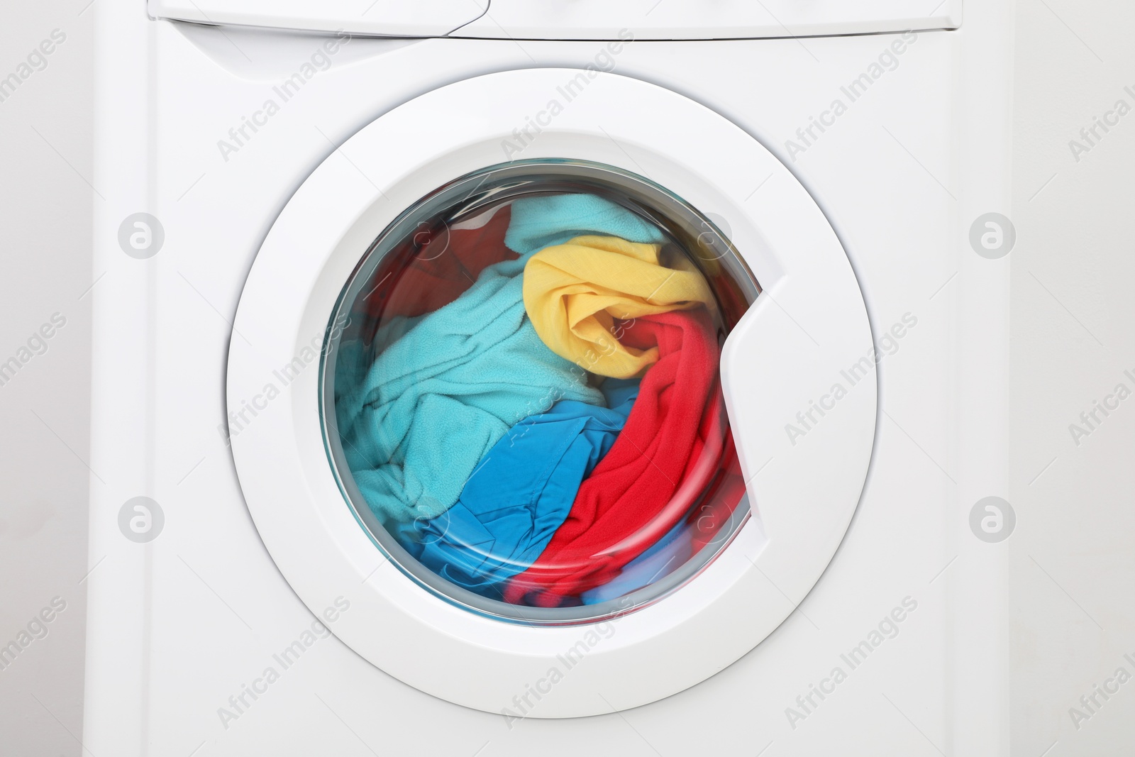 Photo of Washing machine with laundry near light wall, closeup