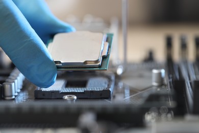 Photo of Man installing computer chip onto motherboard at table, closeup