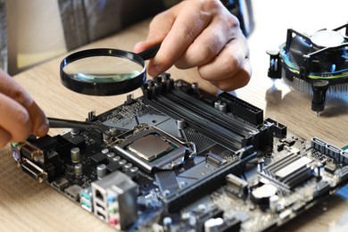 Photo of Man installing computer chip onto motherboard at wooden table, closeup