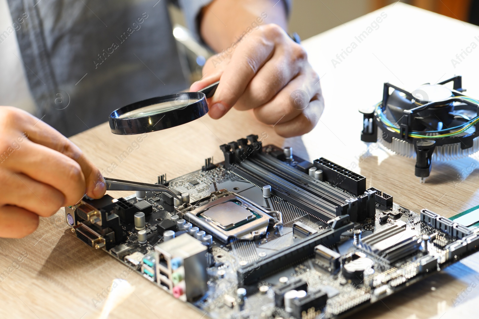 Photo of Man installing computer chip onto motherboard at wooden table, closeup