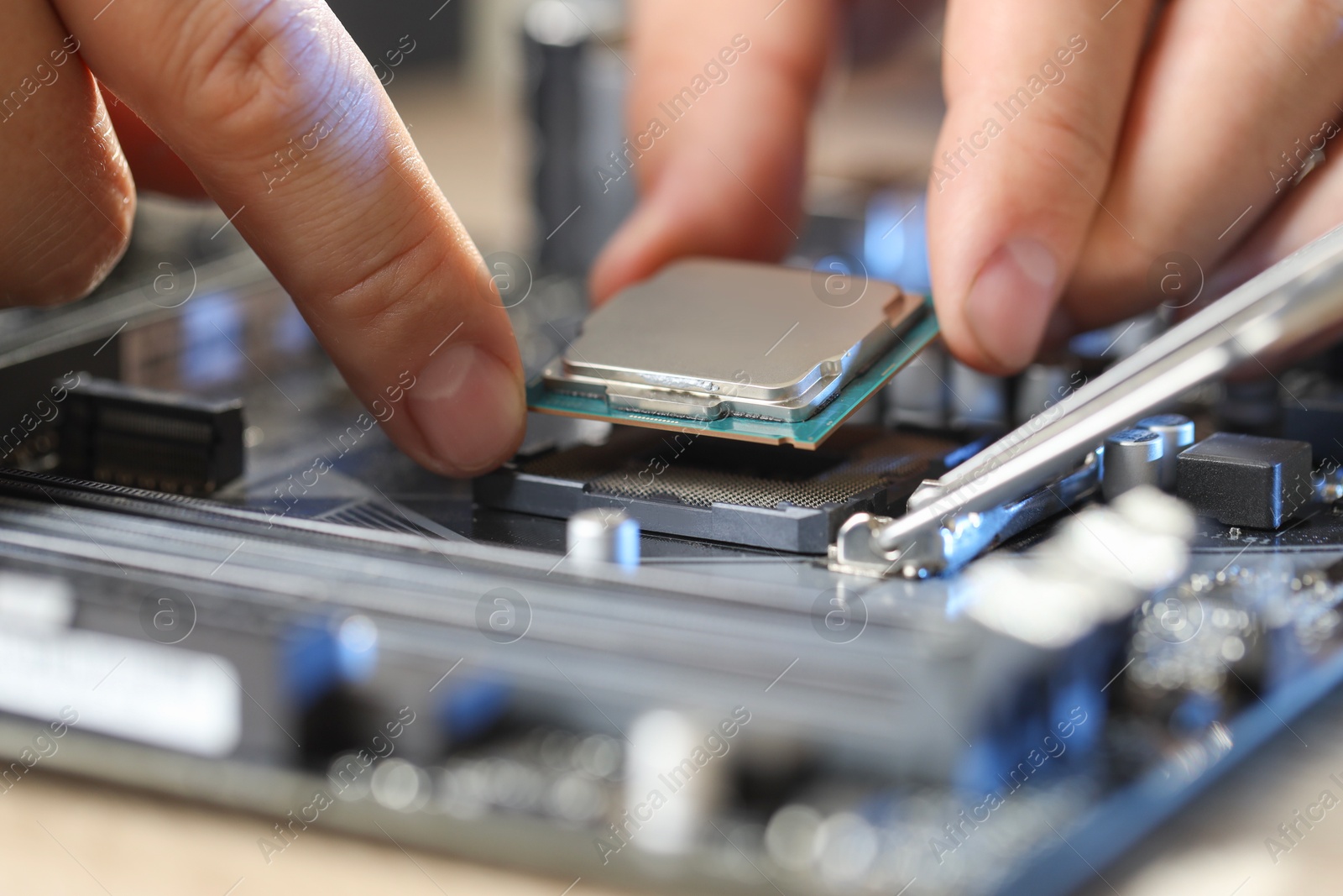 Photo of Man installing computer chip onto motherboard at table, closeup