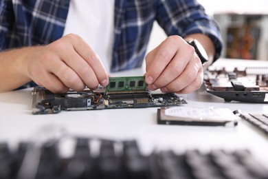 Photo of Man installing computer chip onto motherboard at white table, closeup