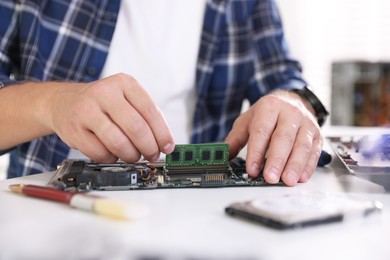 Photo of Man installing computer chip onto motherboard at white table, closeup