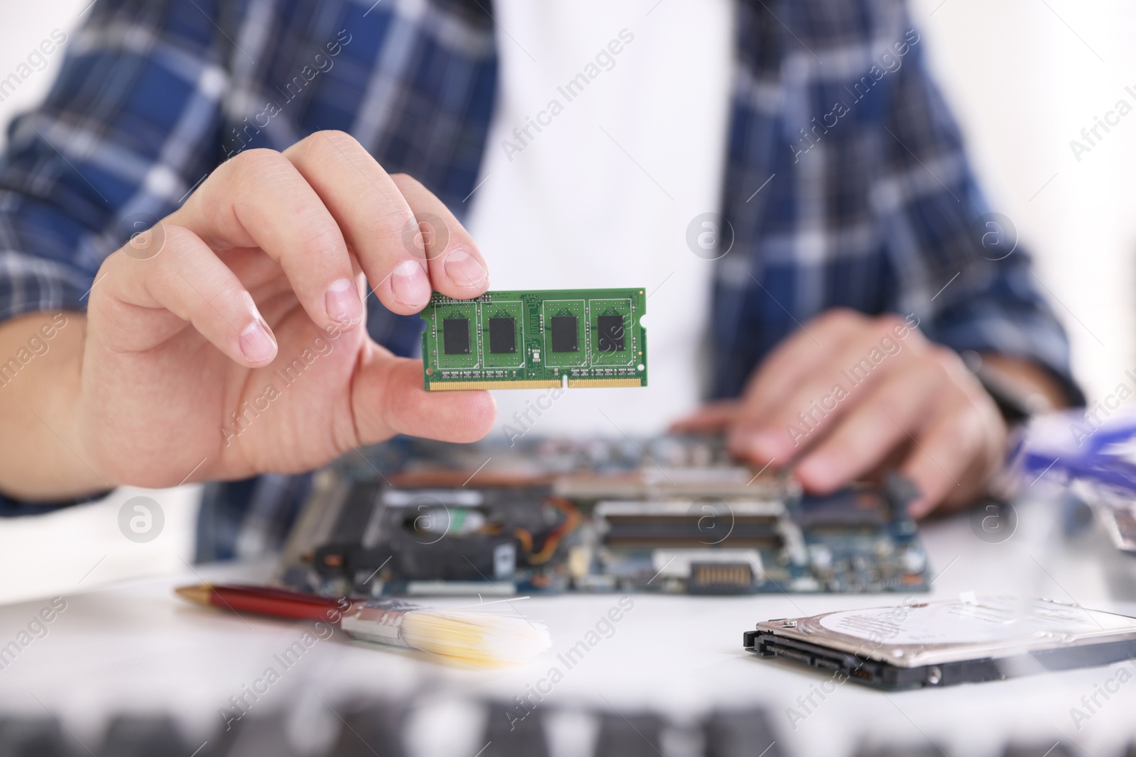 Photo of Man installing computer chip onto motherboard at white table, closeup