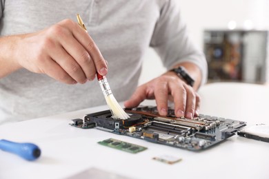 Photo of Man cleaning motherboard with brush at white table, closeup