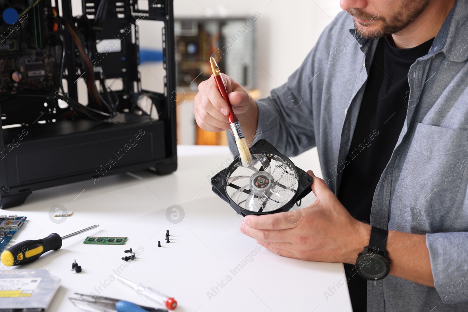 Photo of Man cleaning computer fan at white table, closeup