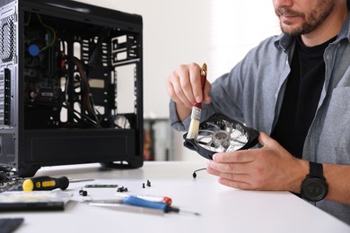 Photo of Man cleaning computer fan at white table, closeup