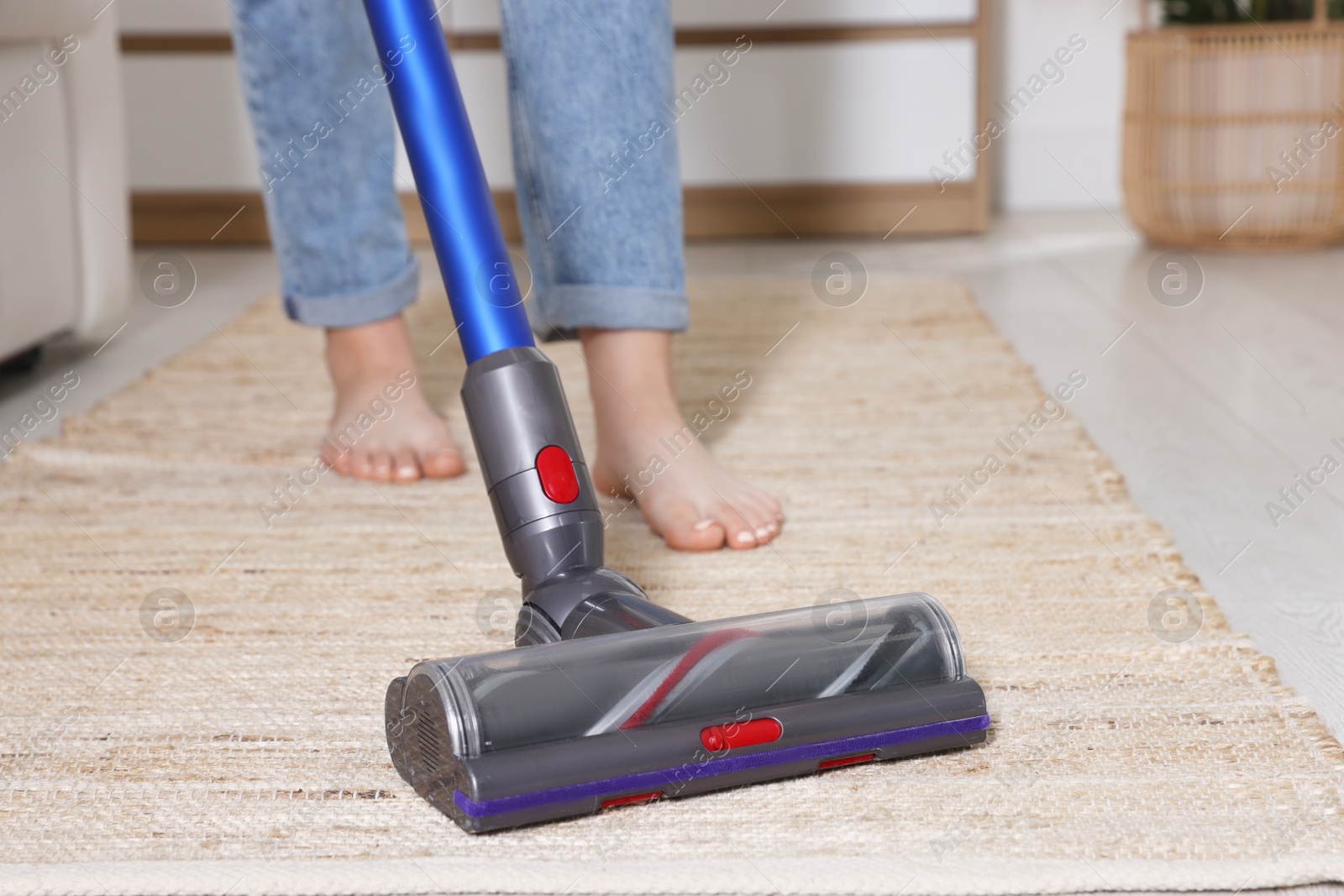 Photo of Teenage girl cleaning rug with cordless vacuum cleaner at home, closeup