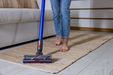 Photo of Teenage girl cleaning rug with cordless vacuum cleaner at home, closeup