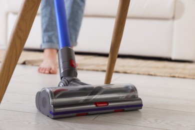 Photo of Teenage girl cleaning floor with cordless vacuum cleaner at home, closeup