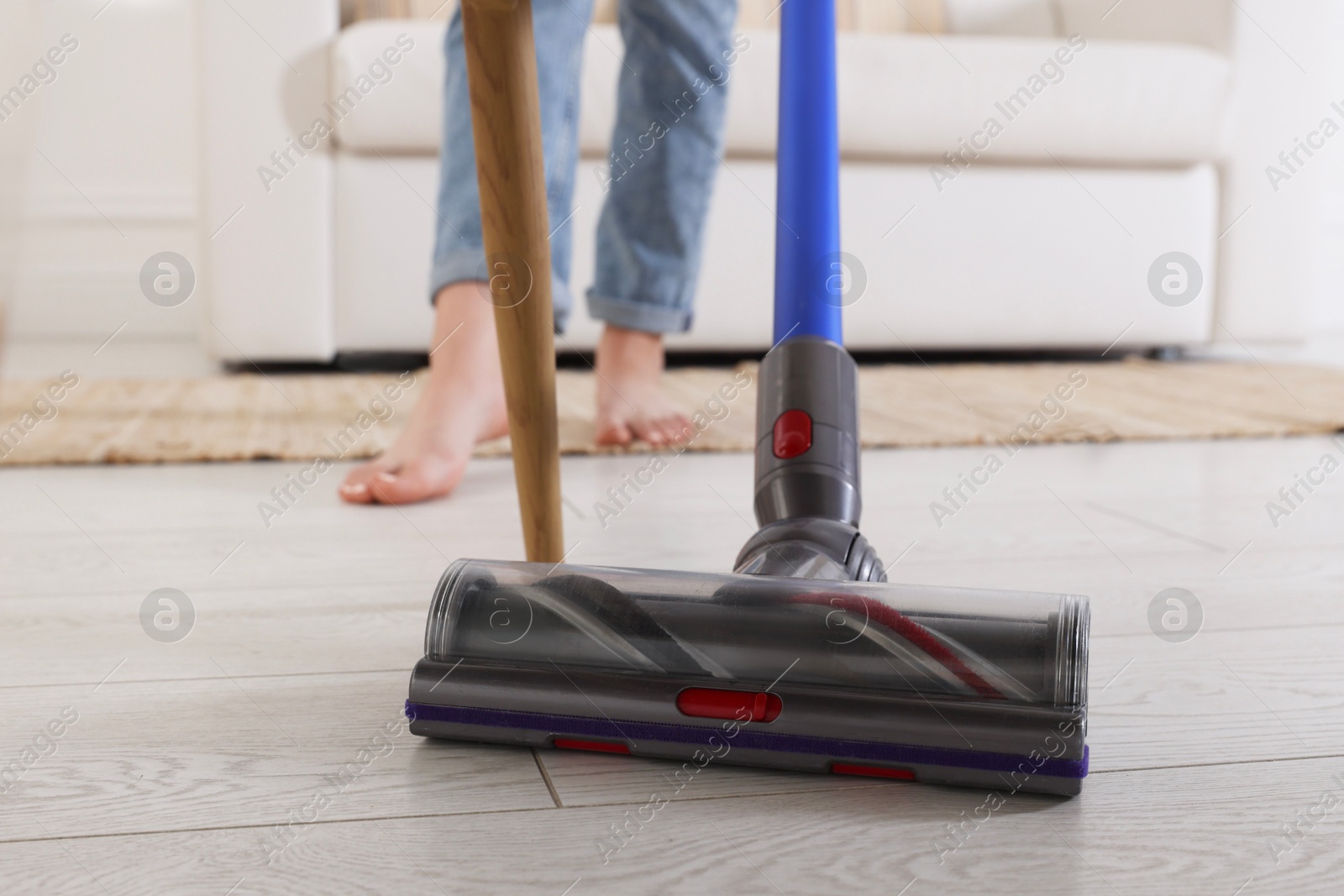 Photo of Teenage girl cleaning floor with cordless vacuum cleaner at home, closeup