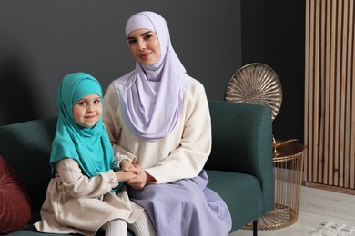 Muslim woman and her daughter sitting on sofa at home