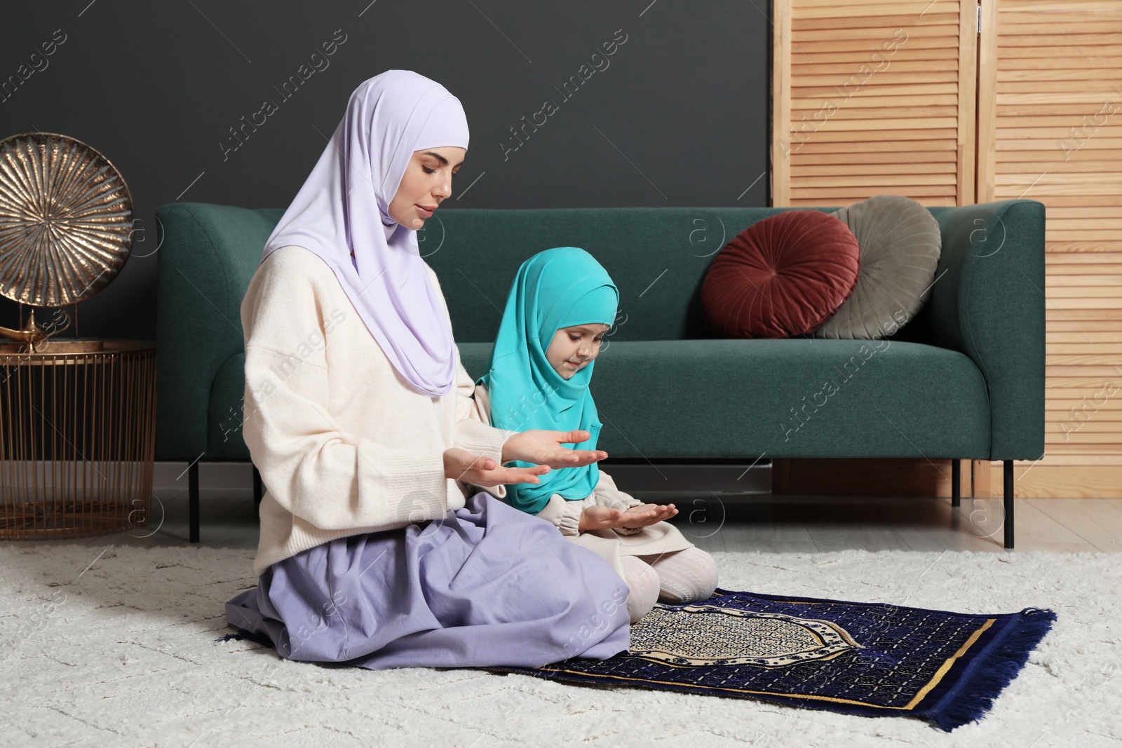 Photo of Muslim woman and her daughter praying on mat at home