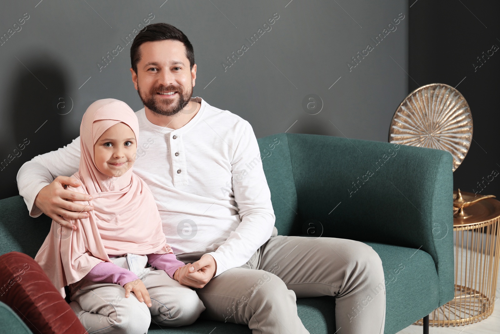 Photo of Muslim man and his daughter sitting on sofa at home