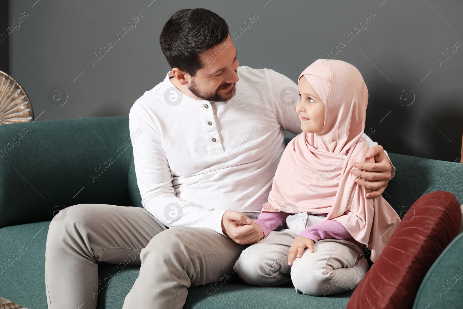 Photo of Muslim man and his daughter sitting on sofa at home