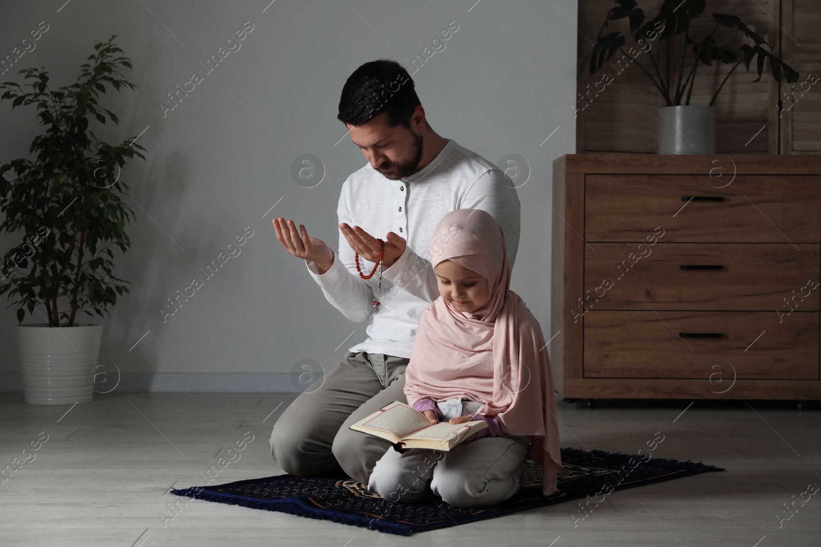 Photo of Muslim man and his daughter with Quran praying on mat at home