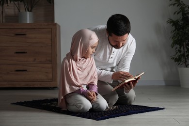 Photo of Muslim man and his daughter with Quran praying on mat at home