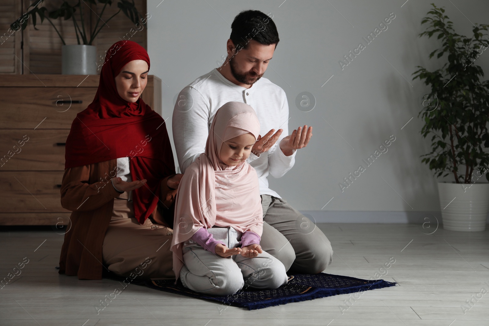 Photo of Muslim family praying on mat at home