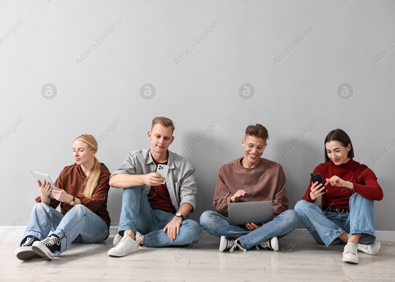 Photo of Group of people using different gadgets near light grey wall indoors. Modern technology