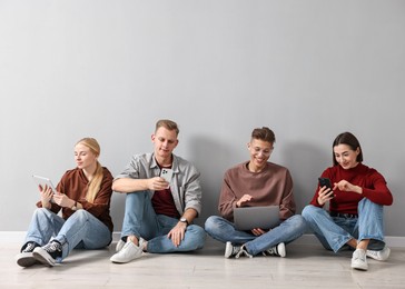 Group of people using different gadgets near light grey wall indoors. Modern technology