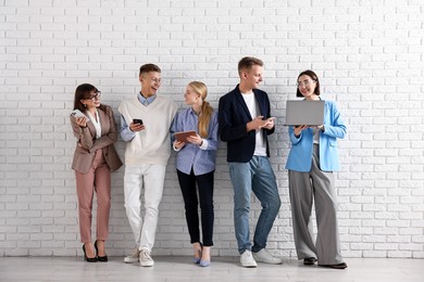 Photo of Group of people using different gadgets near white brick wall indoors. Modern technology