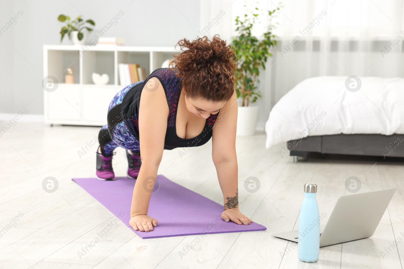 Photo of Plus size woman having fitness training with online coach via laptop at home