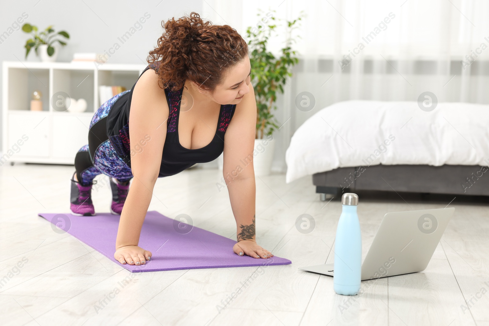 Photo of Plus size woman having fitness training with online coach via laptop at home