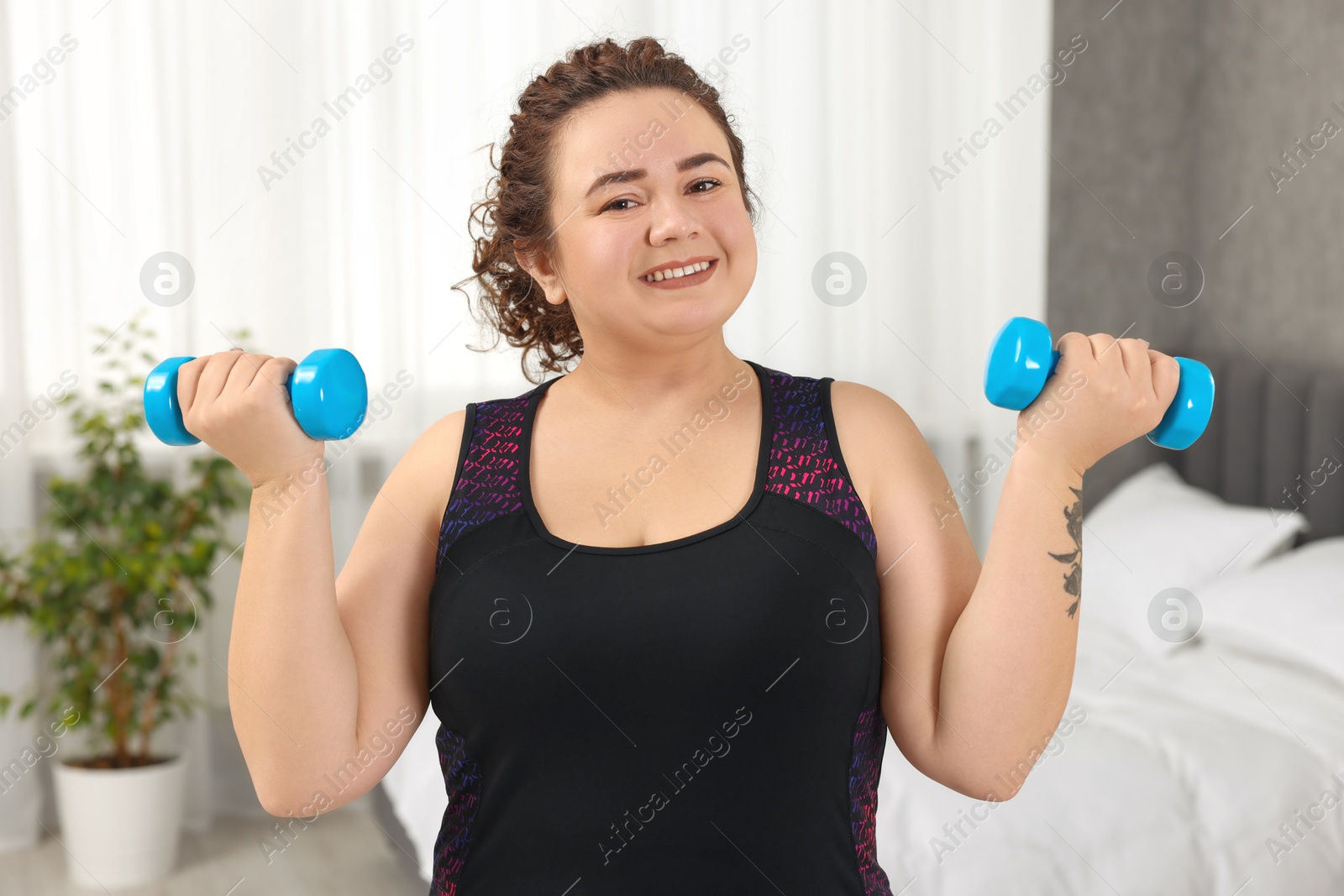 Photo of Plus size woman with dumbbells training at home