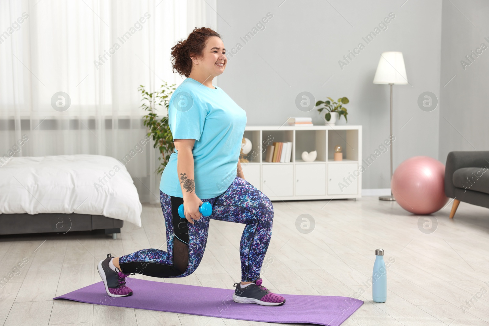 Photo of Plus size woman with dumbbells training at home