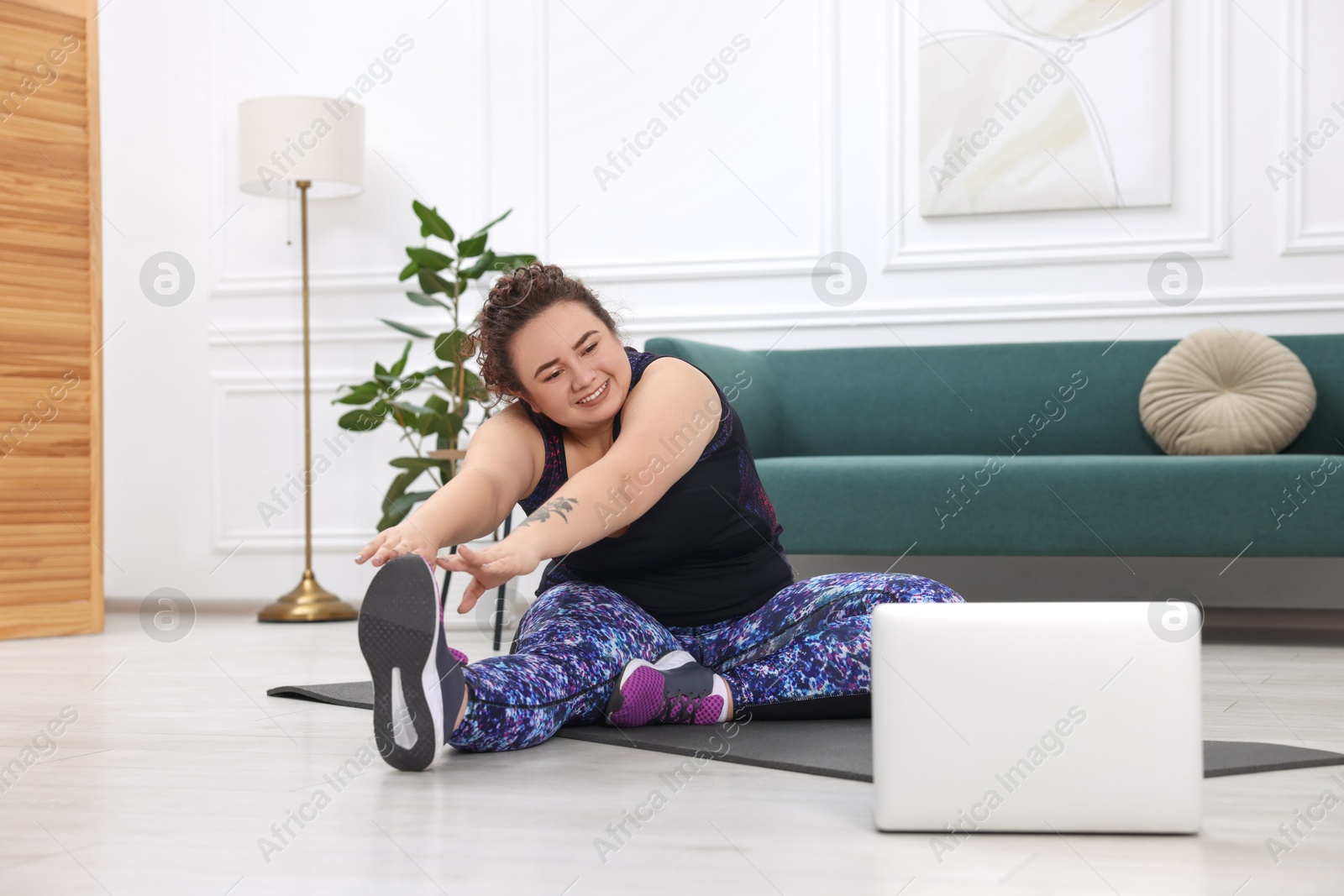 Photo of Plus size woman having fitness training with online coach via laptop at home