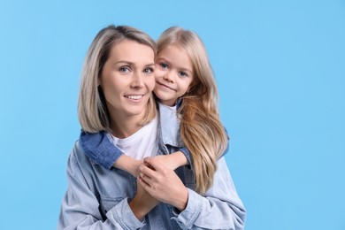 Photo of Cute little girl hugging her mom on light blue background. Happy Mother's Day