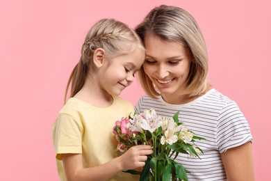 Photo of Little daughter congratulating her mom with bouquet of alstroemeria flowers on pink background. Happy Mother's Day