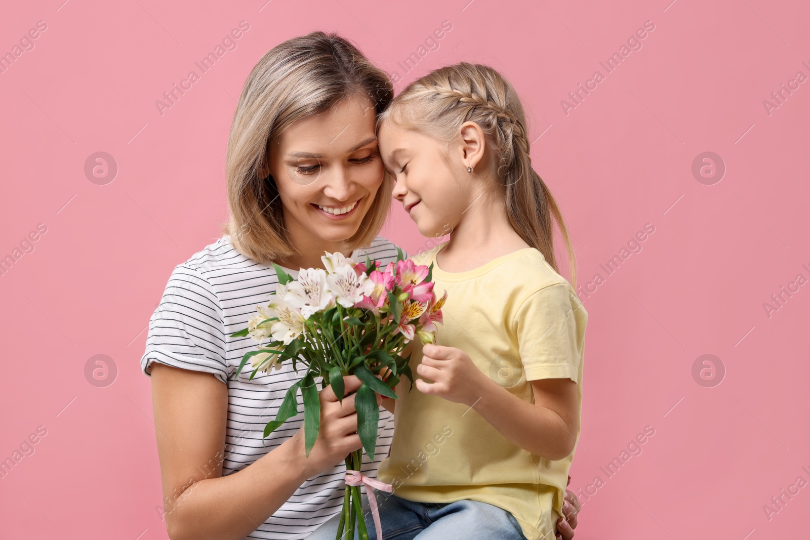 Photo of Little daughter congratulating her mom with bouquet of alstroemeria flowers on pink background. Happy Mother's Day