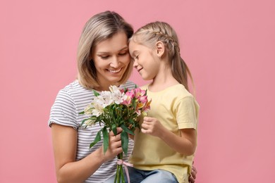 Photo of Little daughter congratulating her mom with bouquet of alstroemeria flowers on pink background. Happy Mother's Day