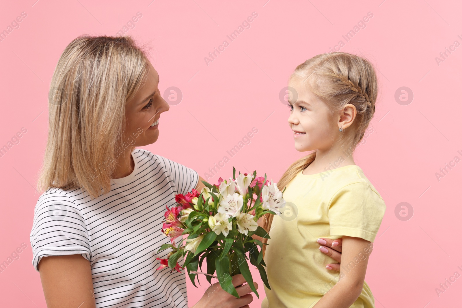 Photo of Little daughter congratulating her mom with bouquet of alstroemeria flowers on pink background. Happy Mother's Day