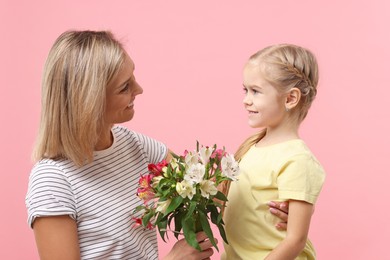 Photo of Little daughter congratulating her mom with bouquet of alstroemeria flowers on pink background. Happy Mother's Day