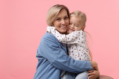 Photo of Cute little girl hugging her mom on pink background. Happy Mother's Day