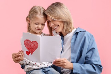 Photo of Happy woman with her daughter and greeting card on pink background. Mother's Day celebration