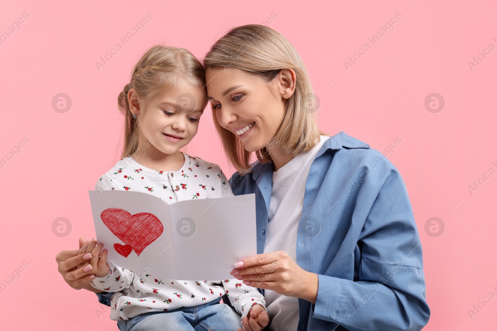 Photo of Happy woman with her daughter and greeting card on pink background. Mother's Day celebration