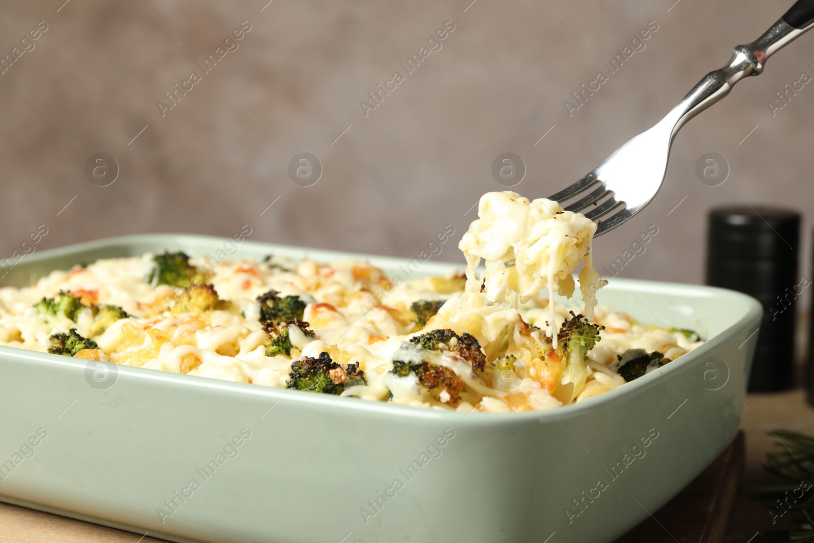 Photo of Taking tasty pasta casserole with fork from baking dish on wooden table, closeup