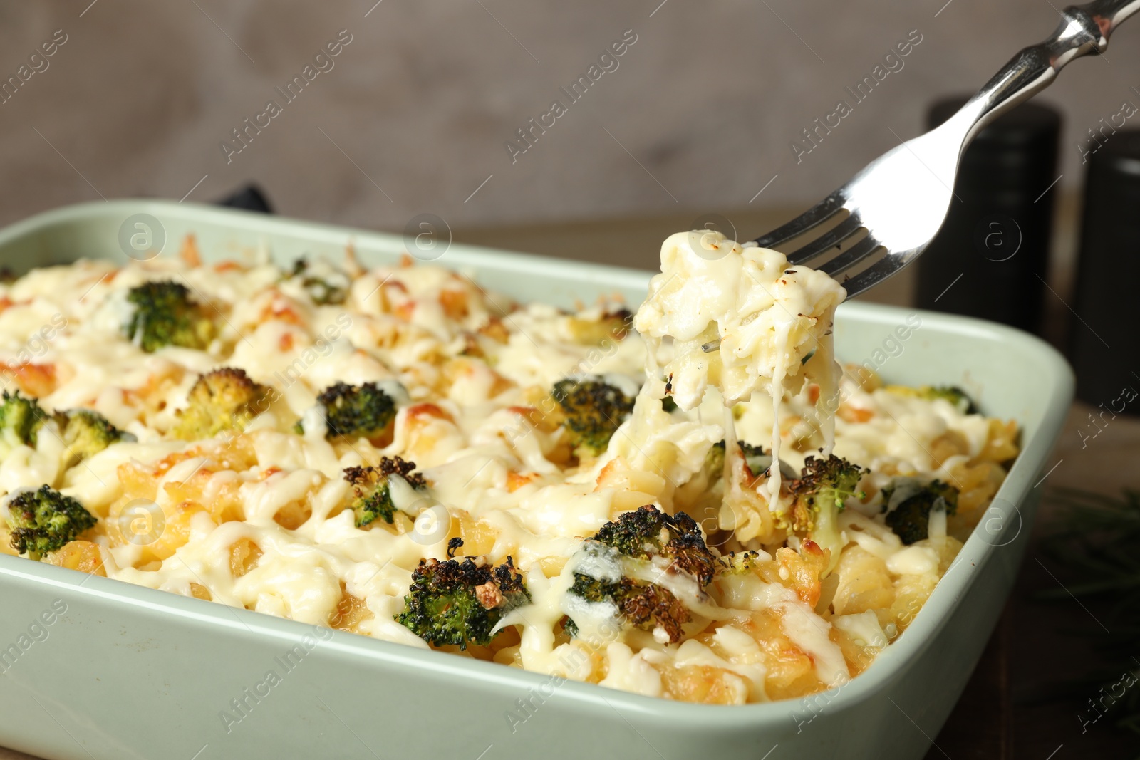 Photo of Taking tasty pasta casserole with fork from baking dish on wooden table, closeup