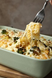 Photo of Taking tasty pasta casserole with fork from baking dish on wooden table, closeup