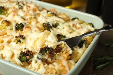 Photo of Taking tasty pasta casserole with fork from baking dish on wooden table, closeup