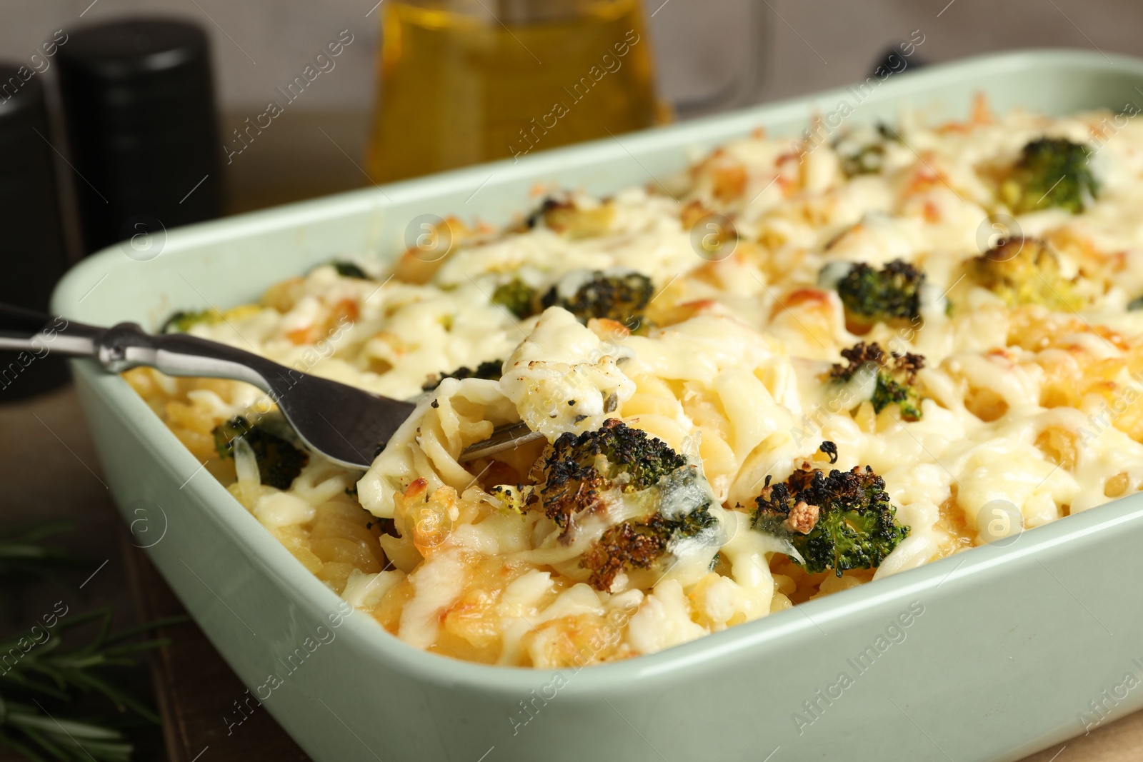 Photo of Taking tasty pasta casserole with fork from baking dish on wooden table, closeup