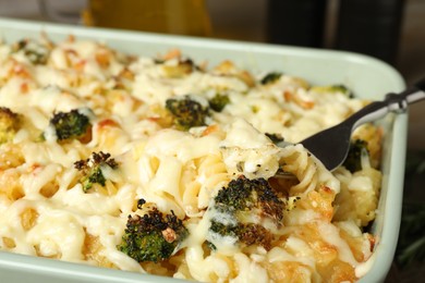 Photo of Taking tasty pasta casserole with fork from baking dish on table, closeup