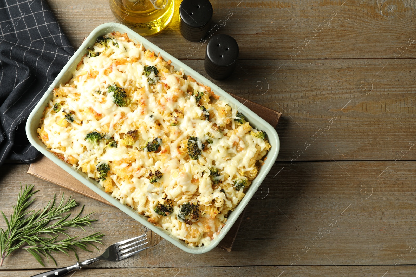 Photo of Tasty pasta casserole with cheese and broccoli in baking dish on wooden table, flat lay. Space for text