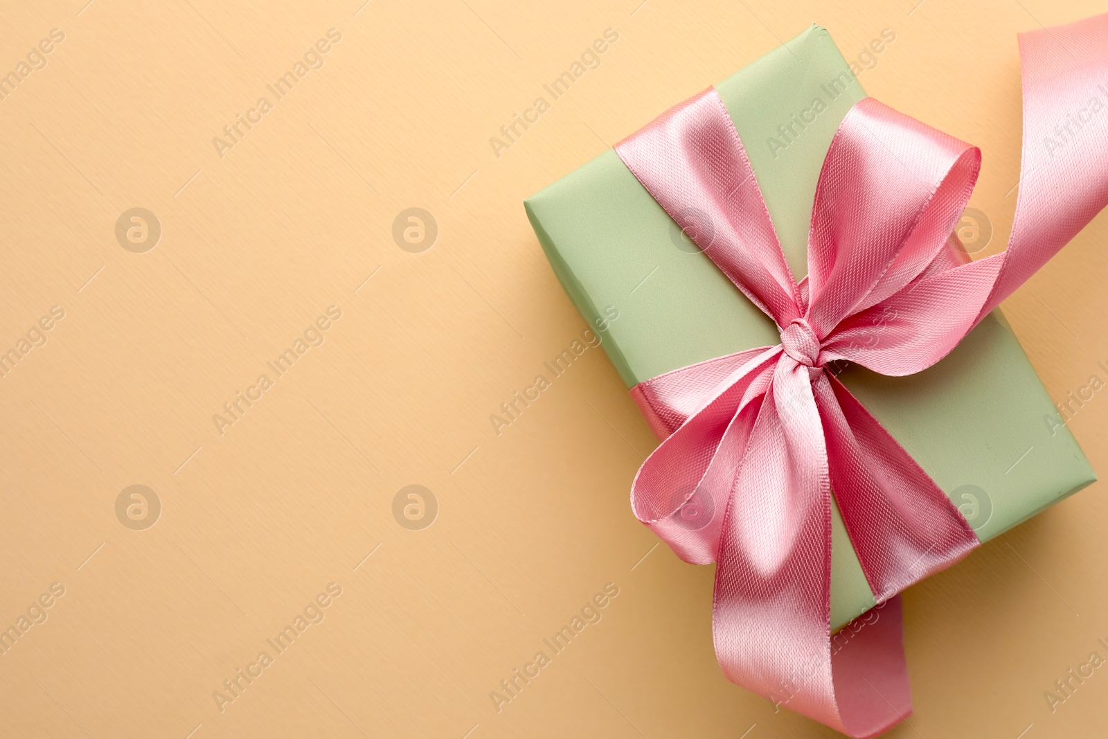 Photo of Beautiful gift box with pink bow on beige background, top view. Space for text