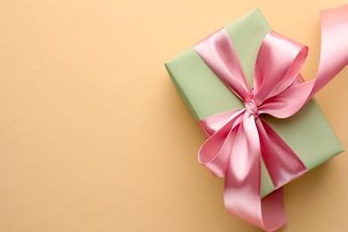 Photo of Beautiful gift box with pink bow on beige background, top view. Space for text